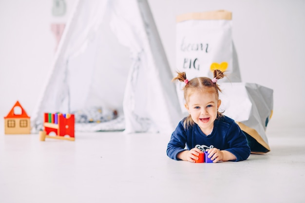 Grappig meisje dat pret in de ruimte van de witte kinderen heeft. Het gelukkige meisje spelen met speelgoed.