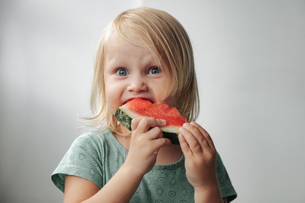 Grappig meisje dat watermeloenclose-up eet. schattig kind met watermeloen binnenshuis. concept van gezonde voeding, zomer. ruimte kopiëren