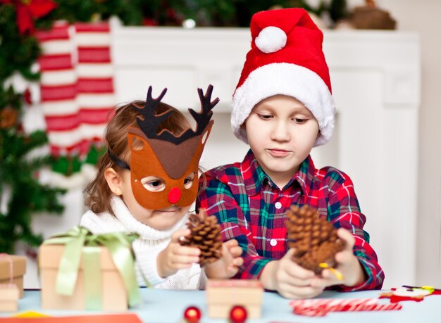 Grappig meisje en jongen in een kersthertenmasker en een kerstmuts met dennenappels