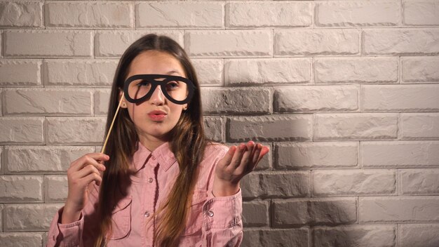 Grappig meisje in roze blouse met een spandoek met zwarte bril op de achtergrond van witte bakstenen muur