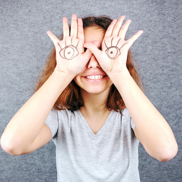 Foto grappig meisje met ogen getekend op haar handpalmen.