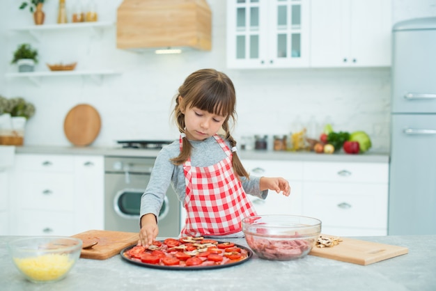 Grappig meisje met staartjes bereidt pizza in de keuken. Kookles voor kinderen.