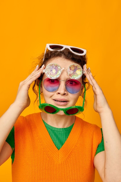 Grappig meisje oranje sweatshirts zonnebril veelkleurige glazen leveren gele achtergrond ongewijzigd