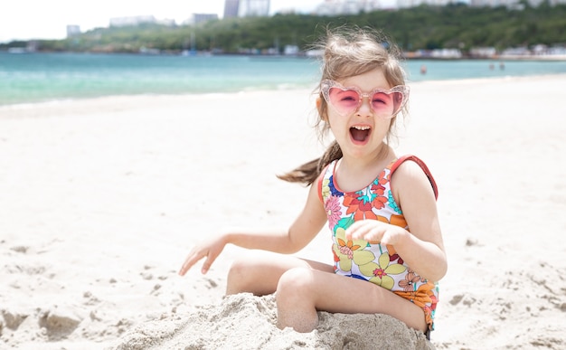 Grappig meisje poseren in zonnebril spelen met zand op het strand. Zomerentertainment en recreatie.