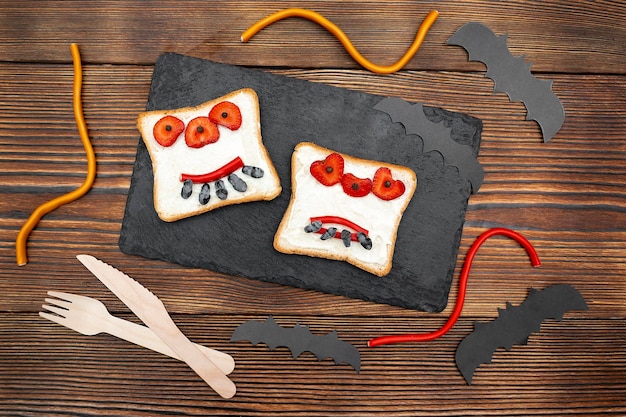 Grappig monster gezicht op halloween sandwich toast brood met boter aardbei snoepjes serveren boardbats op zwarte achtergrond close-up Kids kind zoet dessert ontbijt lunch eten