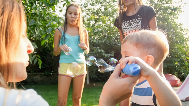 Grappig portret van een gelukkig, vrolijk jong gezin dat zeepbellen blaast en opvangt in de achtertuin van het huis