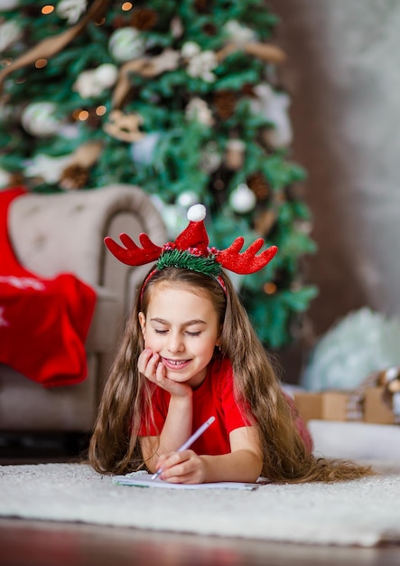 Grappig schattig Kaukasisch meisje schrijft linkshandig een brief aan de kerstman bij de kerstboom