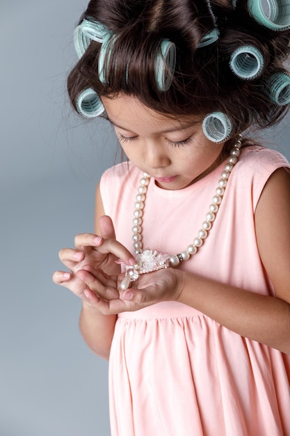 Grappig schattig klein kindmeisje in roze jurk en haarkrulspelden kijkt naar de ketting