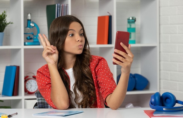 Grappig tienermeisje dat video maakt over selfie met behulp van mobiele telefoon met bloggen over vredesgebaar