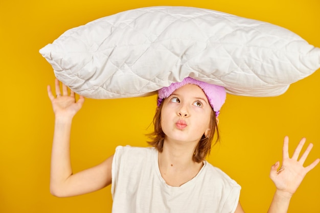 Grappig tienermeisje in witte pyjama met een violet slaapmasker houdt kussen vast