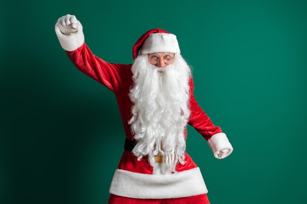 Grappige acteur in kostuum van de kerstman met lange baard gebaren tijdens het dansen op groene achtergrond