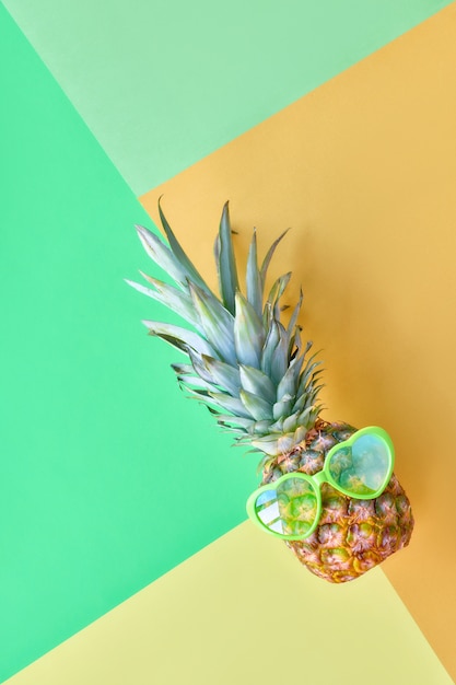 Grappige ananas in hartvormige zonnebril op geometrisch pastel gekleurd papier i