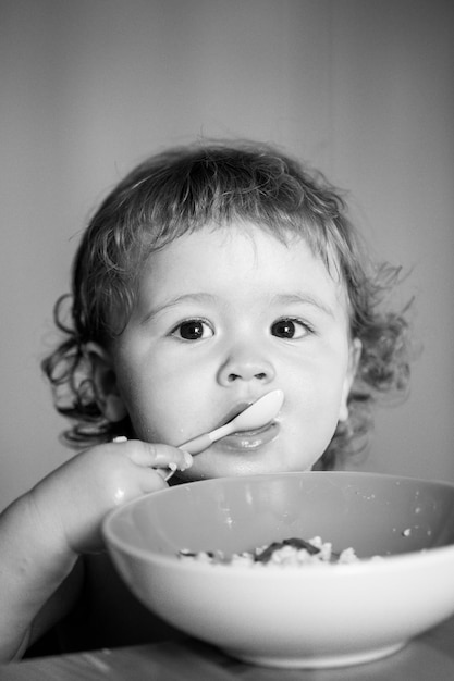 Grappige baby die zelf voedsel eet met een lepel op keuken kindervoeding concept grappig kind gezicht close-up