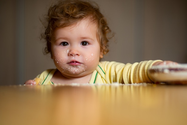 Grappige baby met een lepel en een bord in de keuken thuis.