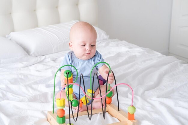 grappige babyjongen in blauwe bodysuit spelen met houten speelgoed op bed