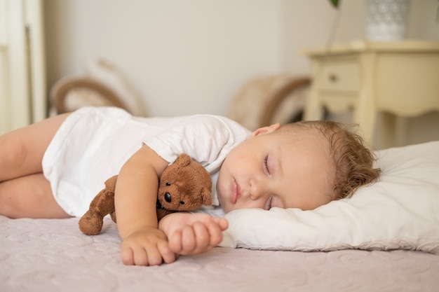 Grappige babyjongen slapen op bed thuis kind knuffelen teddybeer