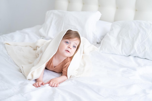 grappige babymeisje glimlachend en liggend op een wit linnen onder deken thuis