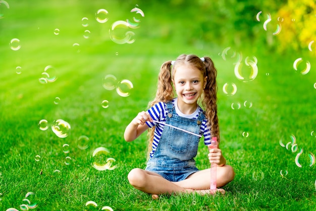 Grappige babymeisje in de zomer op het gazon met zeepbellen op het groene gras met plezier en vreugde ruimte voor tekst