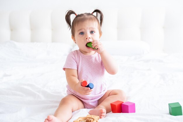 grappige babymeisje in roze bodysuit spelen met kinderen houten kubussen speelgoed op bed