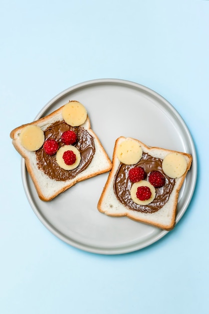 Grappige beer gezicht sandwich toast brood met pindakaas kaas en framboos op plaat blauwe achtergrond Kinderen kind zoet dessert ontbijt lunch eten close-up