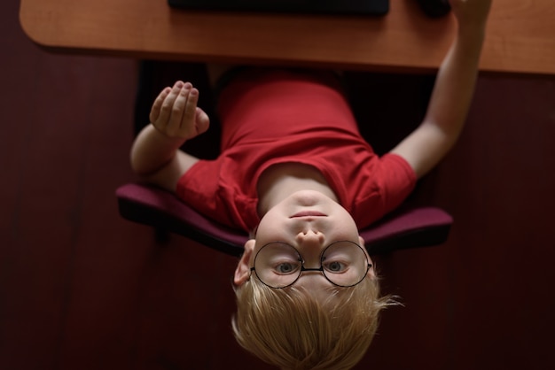 Grappige blonde jongen in glazen die bij laptop rusten. Internet en kleuter.