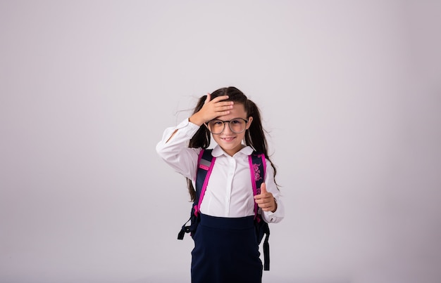 Grappige brunette schoolmeisje in uniform en bril op een witte achtergrond met een plek voor tekst