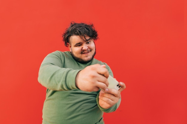 Grappige charismatische jonge zwaarlijvige man heeft plezier met het spelen van games op zijn mobiele telefoon