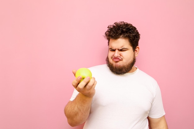 grappige dikke man met een appel in zijn hand en gefrustreerd kijkend naar het fruit en een grappig gezicht trekkend