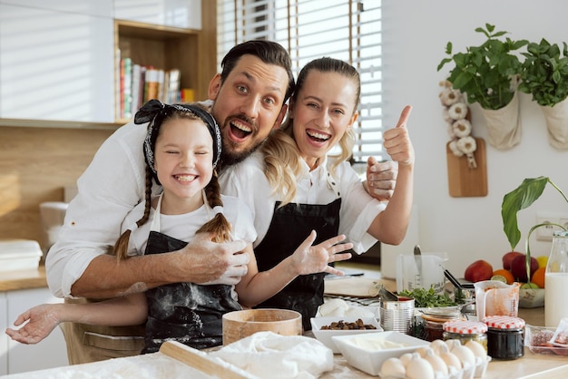 Grappige familie in schorten kijken camera glimlachen Bereide pizza-ingrediënten op houten oppervlak