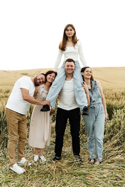 Grappige familie is in het tarweveld. een volwassen dochter zit op de schouders van haar vader, de rest van de gezinsleden glimlachen. een groep autochtonen.