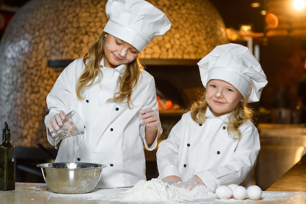 Grappige gelukkige chef-kokmeisjes die bij restaurantkeuken koken