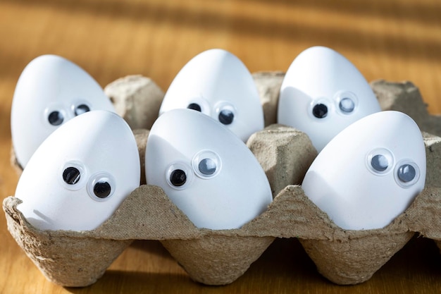 Grappige gezichten op witte eieren in kartonnen doos met biologische kippeneieren op keukentafel close-up grote animatie ogen humor eten en paasvakantie concept