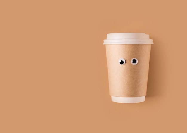 Grappige googly eyes kopje koffie om te gaan papier plat lag op een bruine achtergrond creatief concept kopieerruimte bovenaanzicht