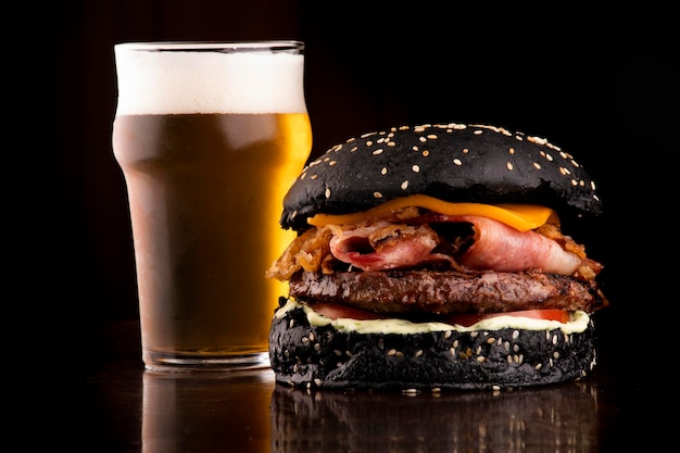 Grappige halloween thema hamburger krokant zwart broodje spek en ui plakjes met sesam op houten tafel geserveerd met halve pint ambachtelijke bier close-up