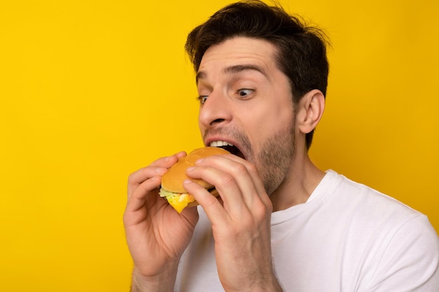 Grappige hongerige man met hamburger bijtende sandwich in studio