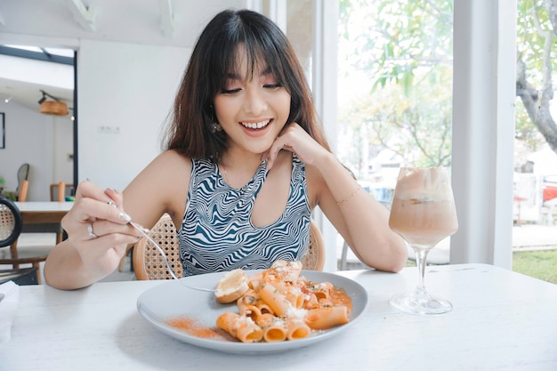 Grappige jonge Aziatische vrouw smakelijke pasta eten in café