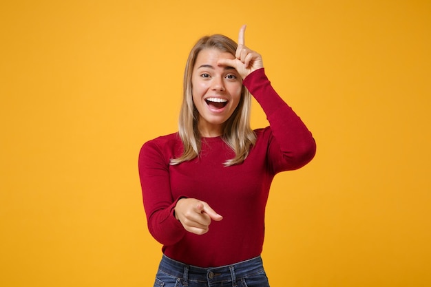 Grappige jonge blonde vrouw meisje in casual kleding poseren geïsoleerd op geeloranje muur achtergrond. Mensen levensstijl concept. Mock up kopie ruimte. Verliezersgebaar tonen, wijsvinger op de camera wijzen.