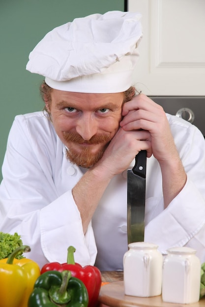 Grappige jonge chef-kok met een mes in de keuken