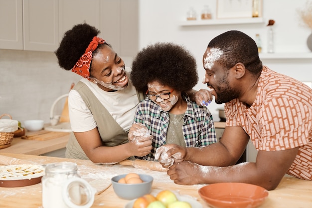 Grappige jonge gezin van drie met bloem op hun gezicht spelen tijdens het koken van zelfgemaakt gebak