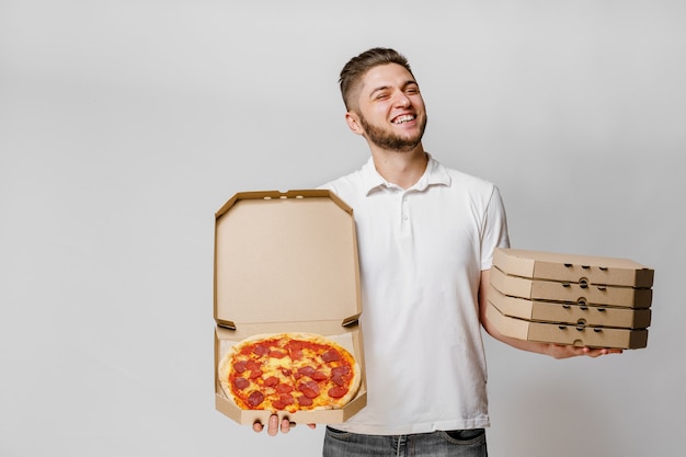 Grappige jonge Kaukasische koerier met pizza en 4 kartonnen doos met pizza's