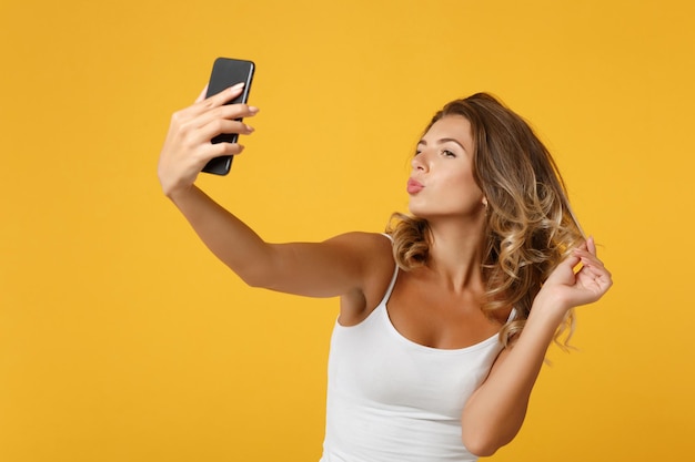 Grappige jonge vrouw meisje in lichte casual kleding poseren geïsoleerd op geeloranje achtergrond. Mensen levensstijl concept. Bespotten kopie ruimte. Selfie geschoten op mobiele telefoon, met luchtkus duck face.