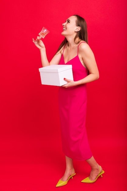 Grappige jonge vrouw met een glas champagne en een cadeau voor het nieuwe jaar op een rode achtergrond