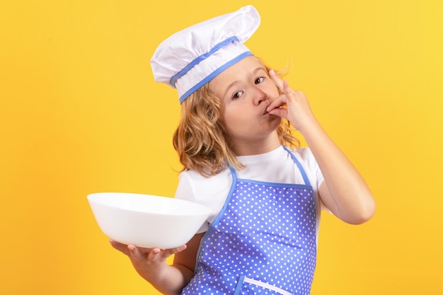 Grappige jongen chef-kok met keukenplaat studio portret Kind in kok uniform Chef-kok jongen geïsoleerd op gele achtergrond Schattig kind om een chef-kok te zijn Kind verkleed als een chef-kok hoed