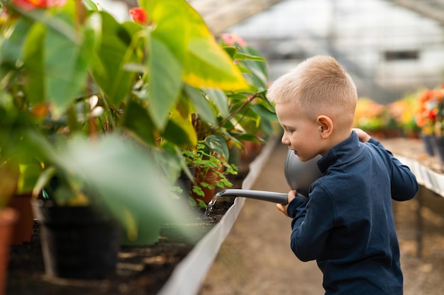 Grappige jongen die bloemen water geeft in de kas