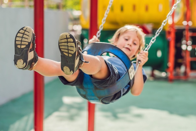 Grappige jongen die plezier heeft met kettingschommel op buitenspeeltuin. kind swingen op warme dag. Actieve vrijetijdsbesteding met kinderen. Jongen die casual kleurrijke schoolkleren draagt