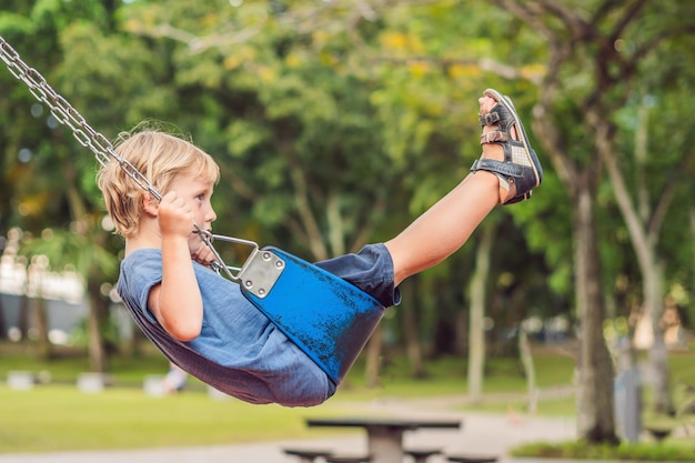 Grappige jongen die plezier heeft met kettingschommel op buitenspeeltuin. kind swingen op warme dag. Actieve vrijetijdsbesteding met kinderen. Jongen die casual kleurrijke schoolkleren draagt