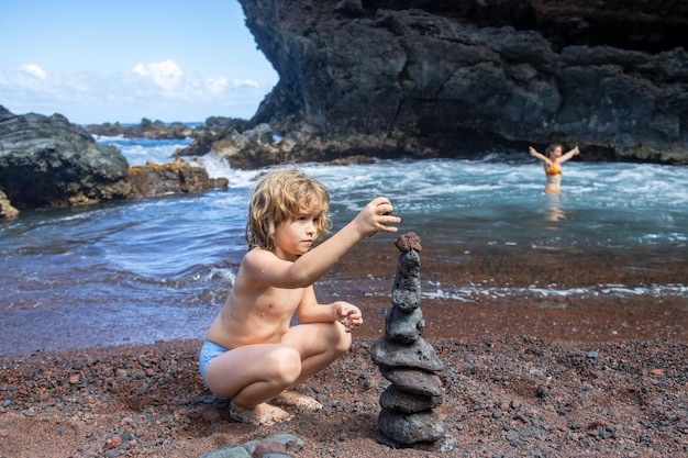 Grappige jongen die stenen piramide maakt op kiezelstrand die stabiliteit zen harmonie balans symboliseert