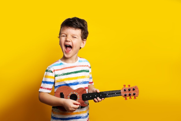 Grappige jongen gitaar spelen een kind met een gitaar op een gele achtergrond in de studio emoties de chi