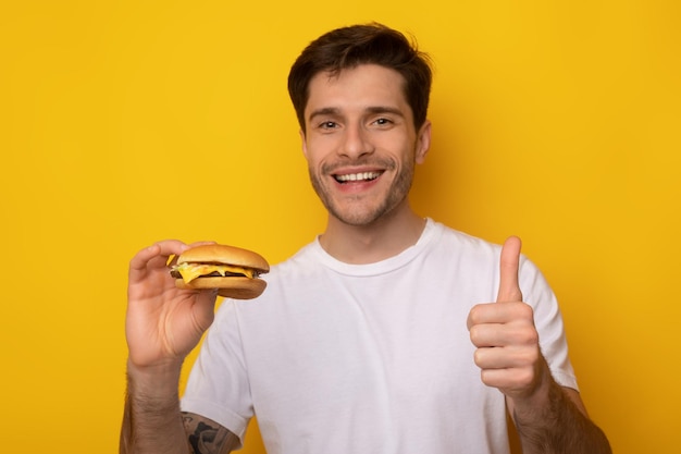 Grappige kerel die hamburger vasthoudt en duim omhoog laat zien
