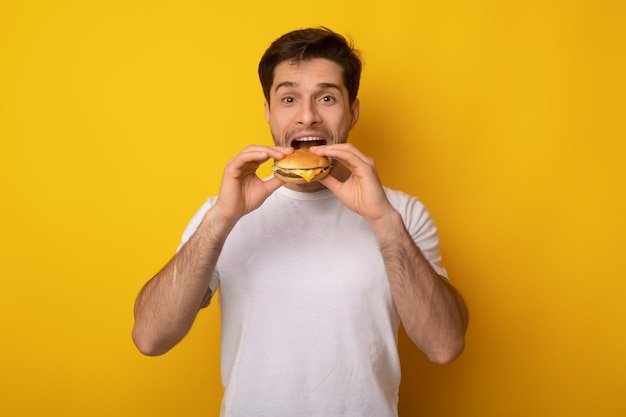 Grappige kerel met hamburger bijtende sandwich in studio